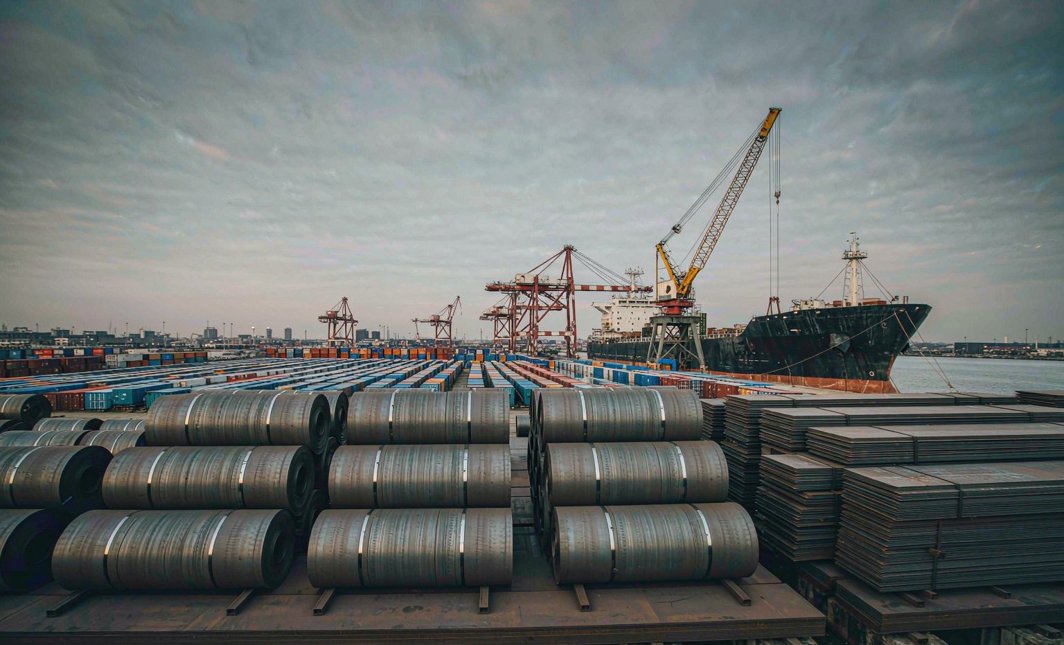 Stacked steel coils and plate bundles awaiting loading at a European port steel terminal