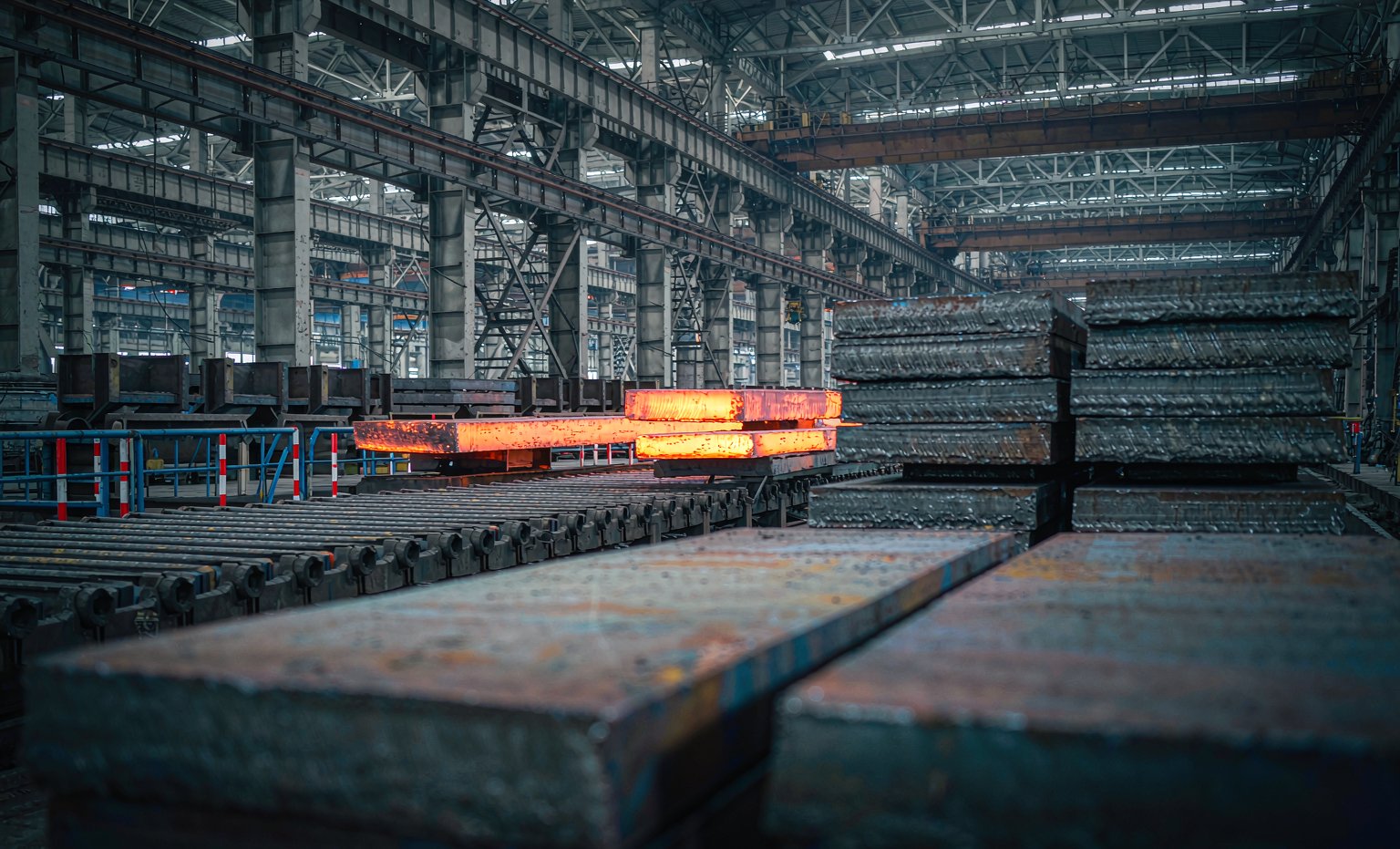 Heavy steel plates stacked in a modern plate mill with glowing slabs on the roller table