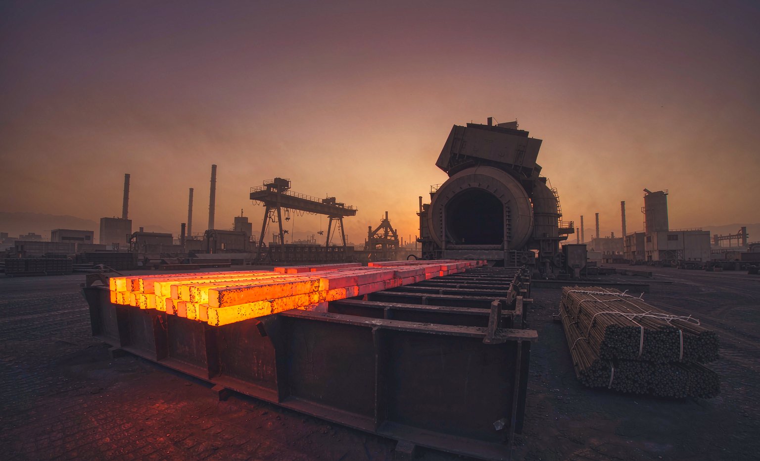 Glowing steel billets cooling in the yard of a steel plant at dusk