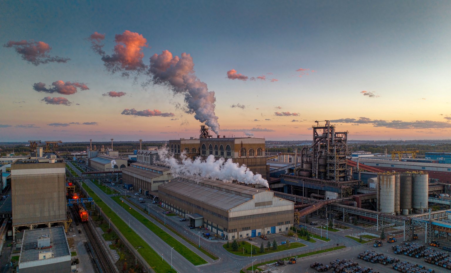 Modern European integrated steel plant with blast furnace and steel coils at sunset