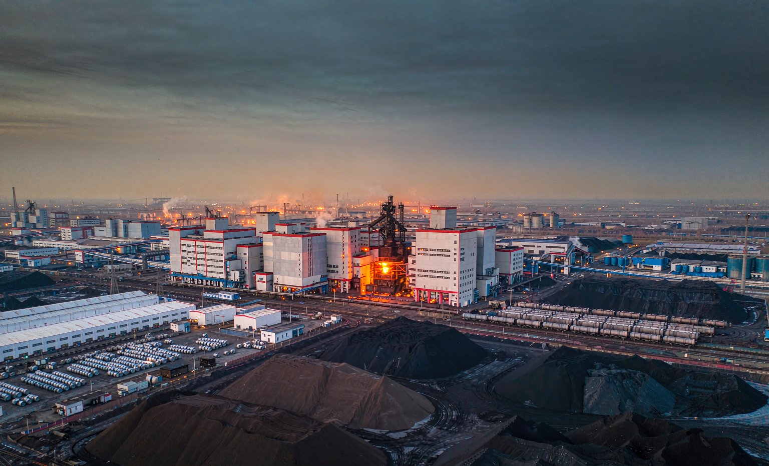 Aerial view of a large modern Chinese integrated steelworks at dusk with blast furnace and coil storage yard